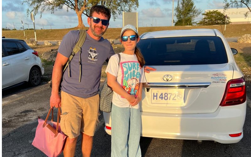 Family posing beside their MasterDrive rental car before exploring Barbados.
