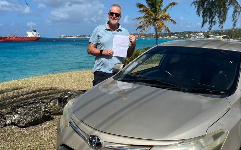 Tourist collecting a MasterDrive rental car with a scenic Barbados coastline in the background.